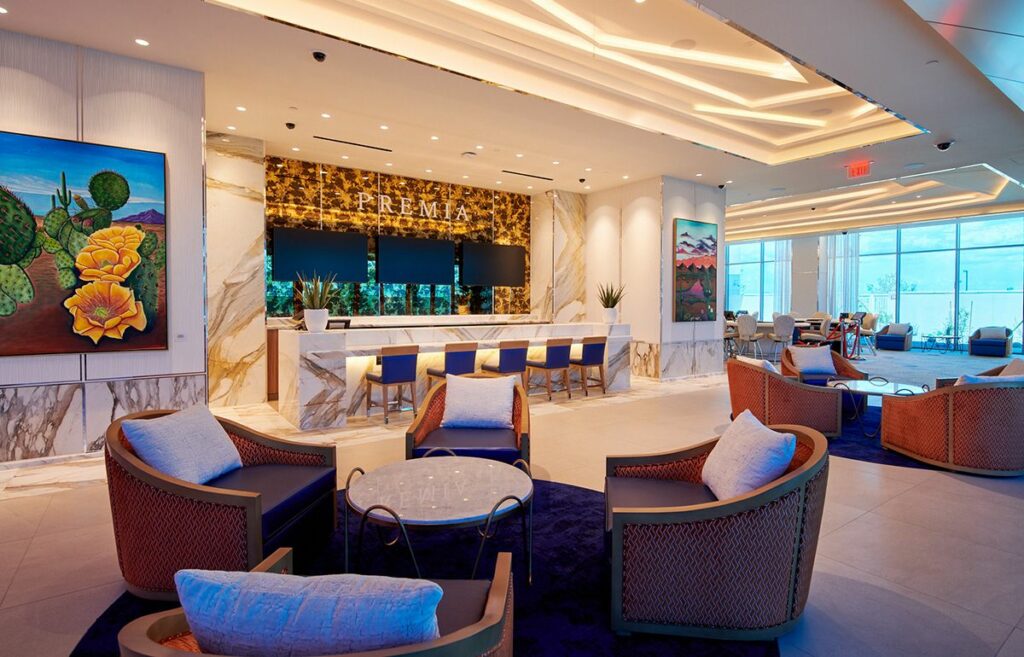 Modern hotel lobby with marble floors, a reception desk labeled "prema," stylish seating areas, and vibrant artwork featuring the "Arizona Project of the Year" on the walls.