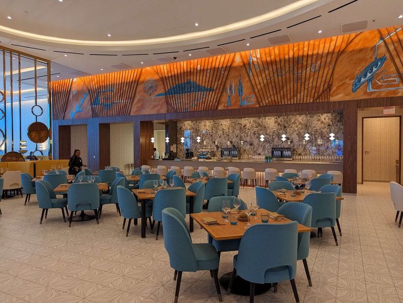 Modern restaurant interior with teal chairs, round tables, and a decorative bar backdrop. Elegant wood paneling with fish designs on the ceiling at the Gila River Santan Mountain Casino.