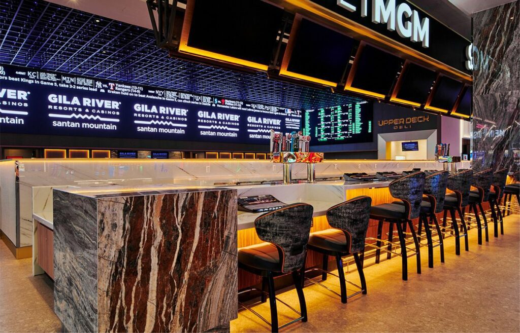 Modern sports bar interior featuring a marble counter, high stools, and multiple screens displaying advertisements for the Gila River Santan Mountain Casino.