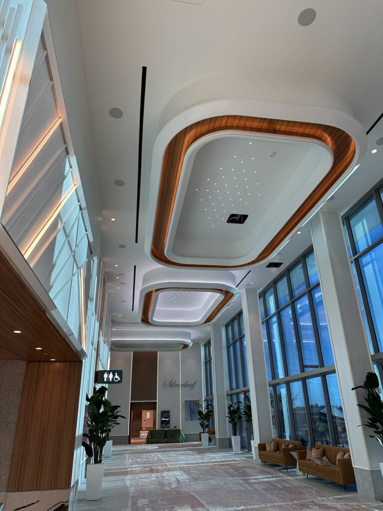 Modern lobby with high ceilings, elegant geometric lighting, large windows, and stylish seating areas under the prominent MKB logo.