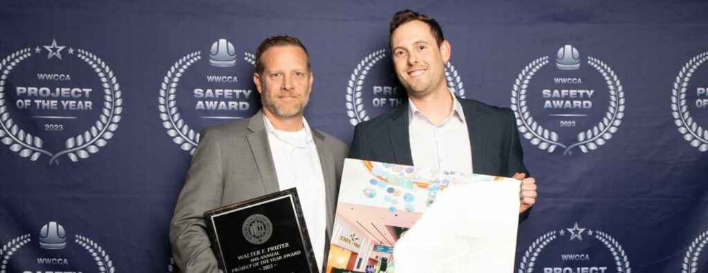 Two men in suits holding awards at a formal event with a backdrop featuring logos and text about the Gila River Santan Mountain Casino and Arizona Project of the Year award.