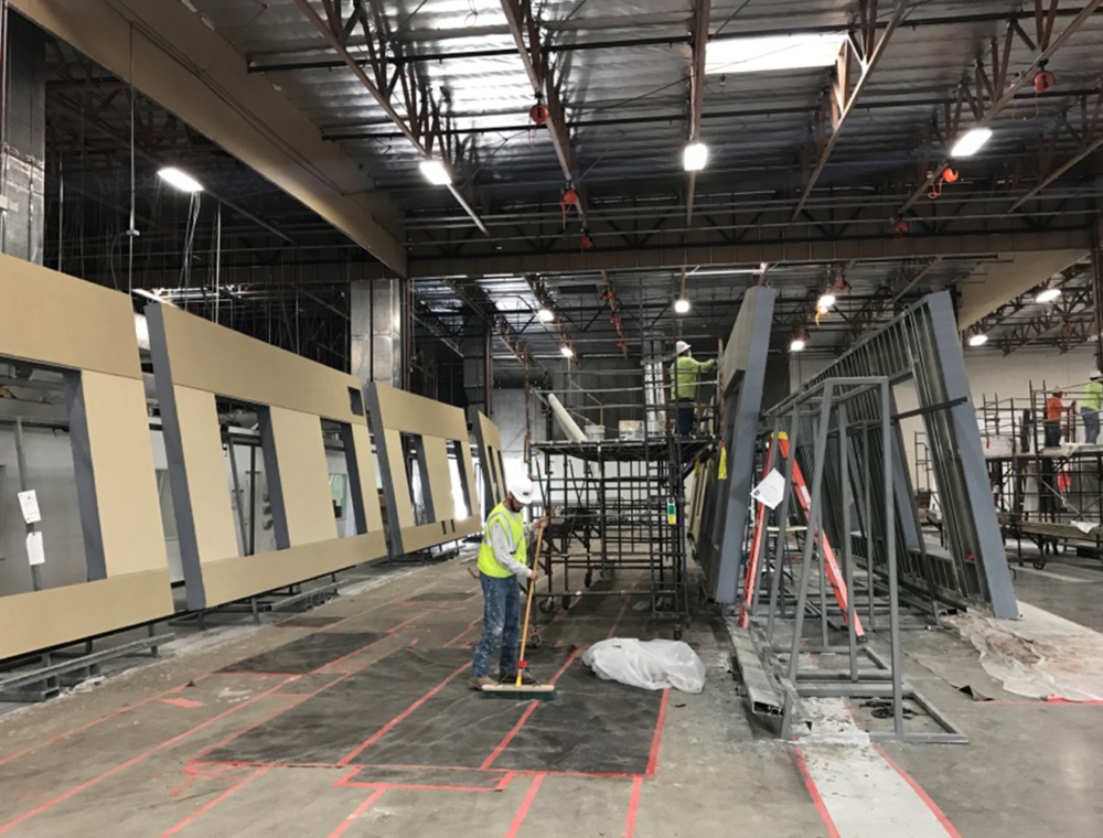 MKB Construction Services worker standing in a large indoor site with metal frameworks and marked floors, overseeing building progress.