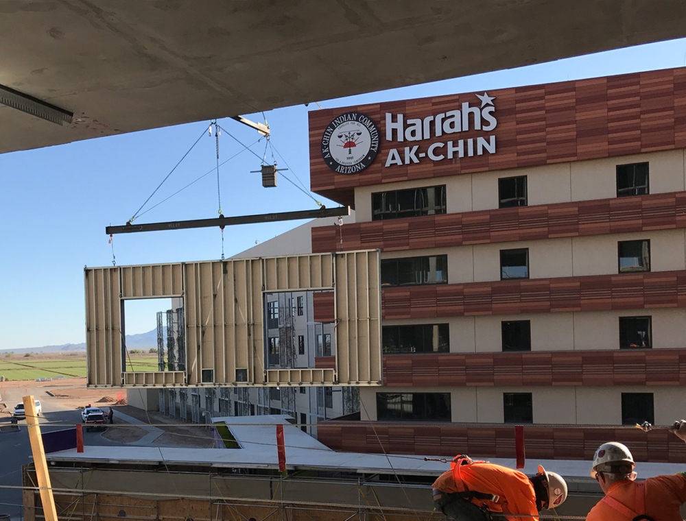 A large modular construction unit being hoisted by a crane beside the Harrah's Ak-Chin Casino building under clear skies, orchestrated by MKB Construction Services.