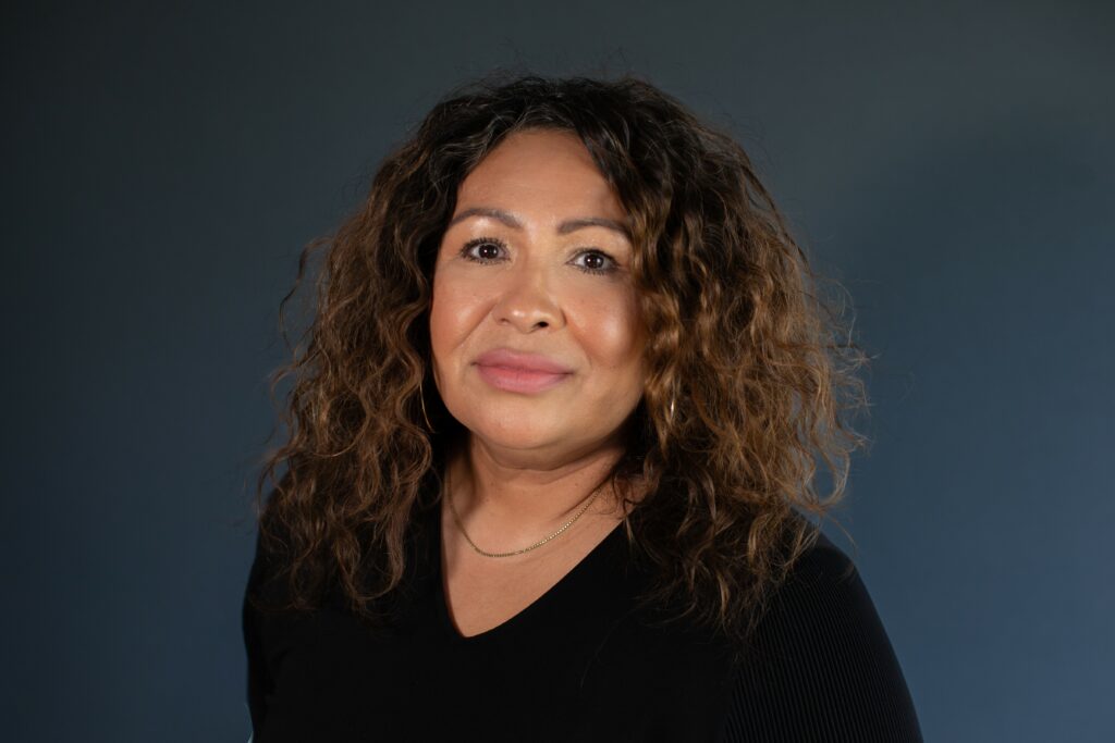 A woman with curly hair, wearing a black top, is posing against a dark blue background, embodying the same confidence and precision that MKB Construction Inc. delivers through their quality services.